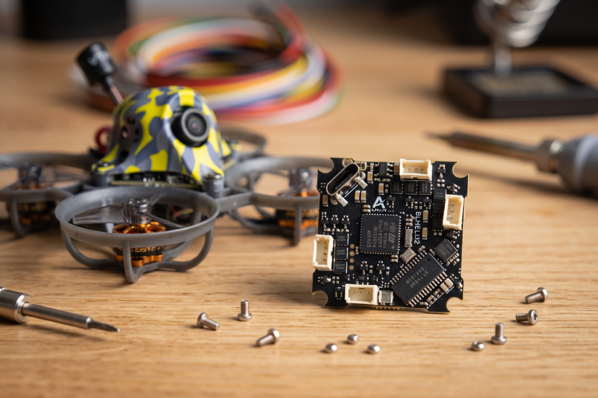 AIO flight controller board with BLHeli_32 ESC next to a tiny whoop drone on a wooden workbench