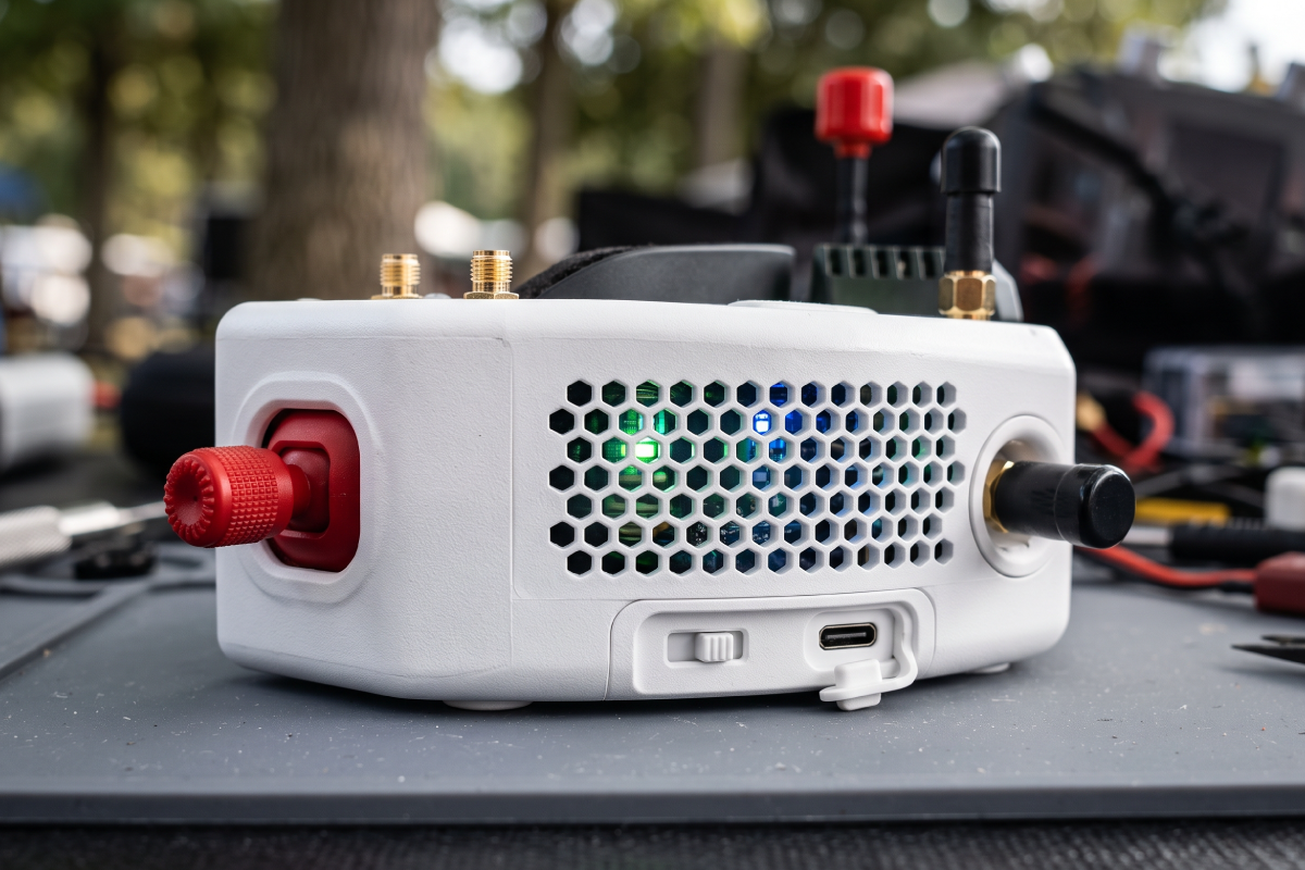 Digital FPV goggles next to white analogue box goggles on a workbench with batteries and antennas
