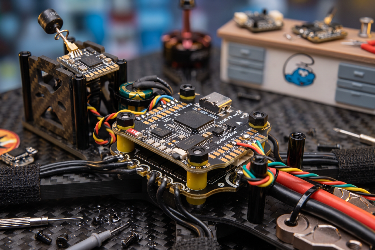 Hands soldering a wire to flight controller pads on an FPV drone stack with an XT60 power lead
